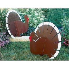 two metal turkeys sitting in the grass next to flowers and bushes, one is brown