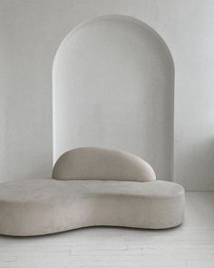 an oval shaped couch sits in the middle of a white room with arched doorways