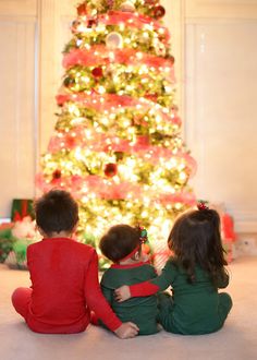 two children sitting next to each other in front of a christmas tree with the words happy holidays