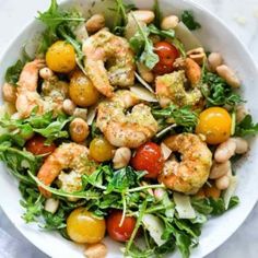 a white bowl filled with shrimp, tomatoes and lettuce on top of a marble table