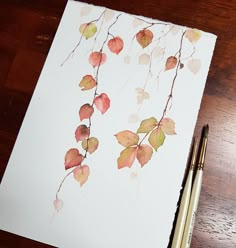 watercolor painting of leaves on white paper with two gold colored pencils next to it