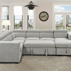 a living room with a large sectional couch and clock on the wall above it's windows