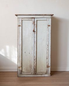 an old white cabinet sitting on top of a hard wood floor next to a wall