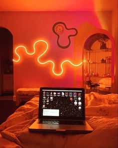 a laptop computer sitting on top of a bed in a room with neon lights above it