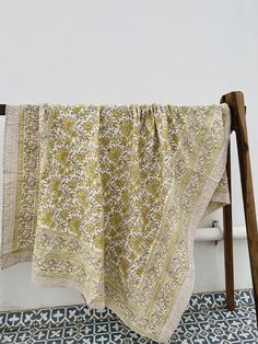 a yellow and white blanket hanging from a wooden chair next to a blue patterned rug