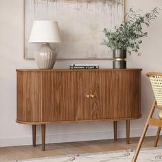 a wooden sideboard with a plant on top and a white lamp next to it