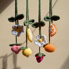 crocheted fruit and flower mobile hanging on a wall next to a window sill