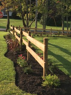 a wooden fence in the middle of a grassy area with flowers and trees around it