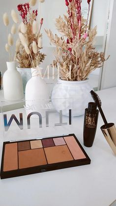 the contents of a makeup set displayed on a white table with flowers in vases