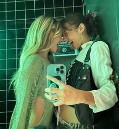 two young women standing next to each other in front of a green tiled bathroom wall