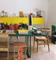 a green table topped with lots of different types of chairs next to a yellow shelf