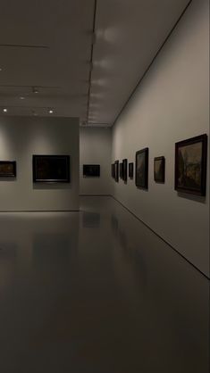 a dimly lit room with paintings on the wall and lights hanging down from the ceiling