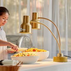 a woman standing in front of a table with bowls of food and a lamp on it