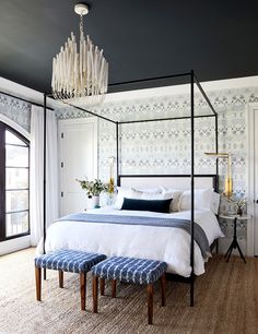 a bedroom with a four poster bed and blue patterned wallpaper on the walls, along with two stools