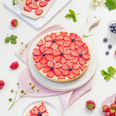 a cake decorated with strawberries and blueberries on top of a white tablecloth