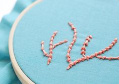 the word love is written in pink thread on a light blue background with a wooden hoop