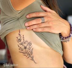 a woman with a flower tattoo on her stomach holding onto the side of her body