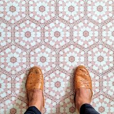 a person standing on a tile floor with their feet propped up against the wall and wearing brown shoes