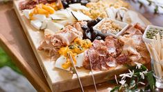 a wooden cutting board topped with lots of different types of cheeses and meats