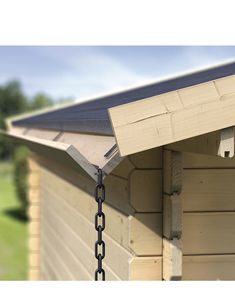 a chain is hanging from the side of a wooden building with grass and trees in the background