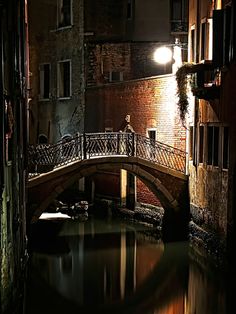 a person standing on a bridge over a canal at night