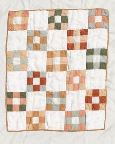 an old patchwork quilt is displayed on a white sheet with brown and green squares