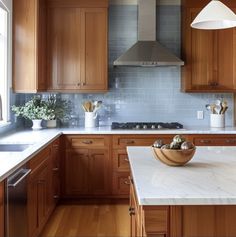 a large kitchen with wooden cabinets and marble counter tops, along with a bowl of fruit on the island