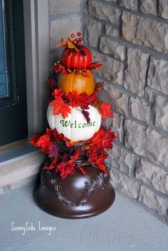 a welcome sign is decorated with pumpkins and autumn leaves on the front door step