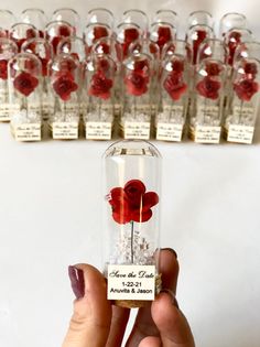 a person holding up a bottle filled with red flowers in front of rows of clear glass bottles