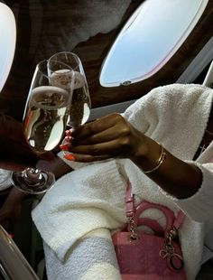 a woman holding two glasses of wine in her hand while sitting on an airplane seat