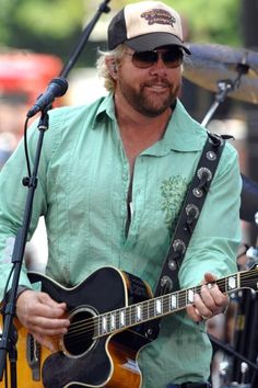 a man with a hat and sunglasses playing an acoustic guitar