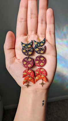 a person's hand with five pairs of earrings on it, all in different colors