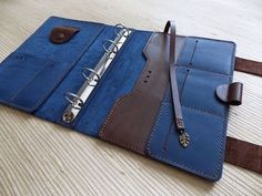 a blue and brown leather folder with two binders attached to the cover, sitting on top of a wooden table