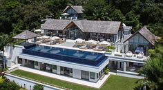 an aerial view of a house with a swimming pool in the foreground and lush vegetation surrounding it