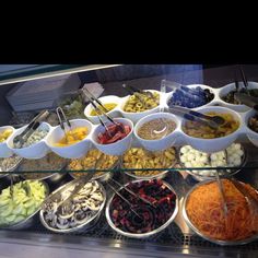 a display case filled with lots of different types of food in bowls and spoons