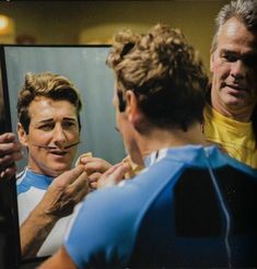 a man is shaving his face in front of a mirror while another man looks on