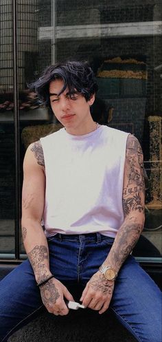 a man with tattoos sitting on top of a black object in front of a building