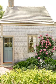 a small brick house with pink flowers in the front yard and blue door on one side