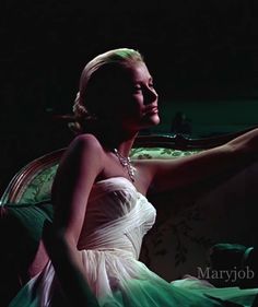 a woman in a white dress is sitting on a couch with her arm around the chair