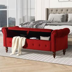 a red bench sitting on top of a wooden floor next to a bed in a bedroom