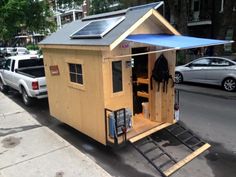 a small wooden house with a solar panel on it's roof is parked next to a sidewalk