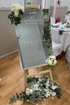 an easel with flowers and greenery on it in front of a wedding sign