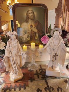 two statues are on display in front of a painting and candle holders with flowers around them