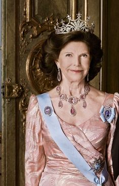 an older woman wearing a tiara in front of a golden door with a blue sash around her neck