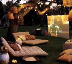 an outdoor movie is set up in the grass with lights strung over it and pillows on the ground