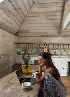 a woman sitting at a wooden table with a laptop and cup in front of her