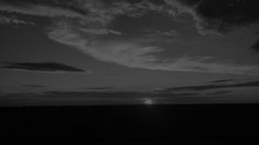 black and white photograph of the sun setting over an open field with clouds in the sky