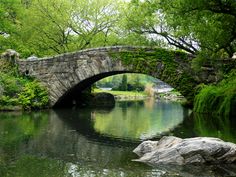 a stone bridge over a river surrounded by lush green trees