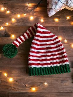 a red and white striped hat sitting on top of a wooden floor next to christmas lights