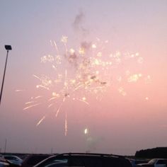 fireworks are lit up in the sky above parked cars at sunset or dawn on a parking lot